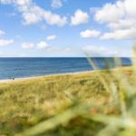 Strand mit Dünen und blauem Meer unter einem wolkenverzierten Himmel.