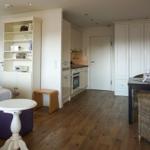 Wohnung mit Schlafzimmer, Küche und Essbereich. Holzboden und weiße Möbel.