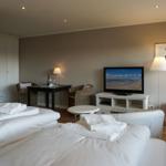 Zwei Betten mit weißen Laken, Fernseher und Sitzgelegenheiten im Zimmer.