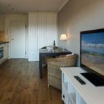 Wohnbereich mit TV, Esstisch und Küchenbereich. Holzfußboden und weiße Möbel.