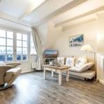 Wohnzimmer mit Sessel, Sofa, Kamin und TV. Holzboden und große Fenster.