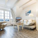 Wohnzimmer mit Sofa, Fernseher und Kamin. Holzfußboden und große Fenster.