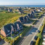 Aerial view of coastal village with red houses, green fields, and ocean in background.