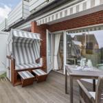 Terrace with beach chair, table, and chairs. Glass window leads to interior space.