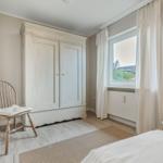 Bedroom with wardrobe, chair, and window with curtains.