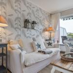 Living room with sofa, chair, and table. Wallpaper with palm leaves. View onto balcony.