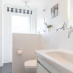 Bathroom with sink, toilet, and shower. Window with checkered curtain.