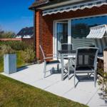 Terrace with table, chairs, and lounge under awning beside red brick house.