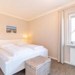 Bedroom with white bed, bedside lamps, and window with curtain.