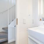 Badezimmer mit Waschbecken und Spiegel. Treppenhaus im Hintergrund.