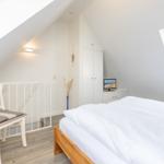 Schlafzimmer mit Dachschrägen, weißer Bettwäsche und Holzbett. Fenster und Stuhl sichtbar.