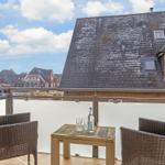 Terrace with table and two chairs, view of rooftops and street.