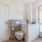 Toilet room with window, white door, and cabinet.