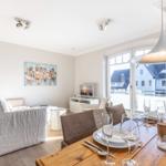 Dining room with wooden table and seating. Corridor to living room with TV.