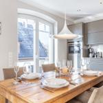 Dining area with wooden table and chairs. Kitchen with gray cabinets and window view.
