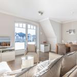 Living and dining area with TV, sofa, and table. View of the beach through windows.