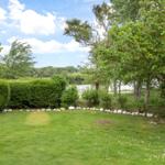 Green garden with stone border, trees, and view of a lake.