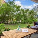 Terrace with table, lounge chair, and garden. Blue beach chair and green plants.