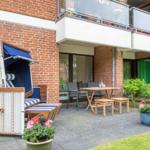 Terrace with beach chair, table, chairs, and plants in front of brick house.