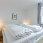 Bedroom with white bed, bedside table, and window.