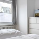 Bedroom with white bed, window with blinds, and TV on dresser.