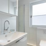 Bathroom with sink, shower, and window with blinds.