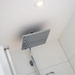 Shower area with ceiling-mounted showerhead and white tiles.