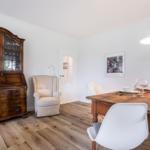 Dining room with wooden table, chairs, and antique cabinet. White walls and wooden floor.