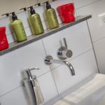 Badezimmer mit Waschbecken, Wasserhahn und Pflegeprodukten auf Arbeitsplatte.