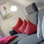 Grauer Sofa mit roten Kissen und einer Stehlampe im Hintergrund.