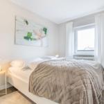 Schlafzimmer mit Bett, Wandbild und Fenster mit weißen Vorhängen.