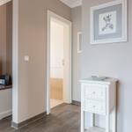Flur mit weißen Möbeln und Bild an der Wand. Tür führt in Bad.