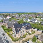 Haus mit Solaranlage, umgeben von Grün und Straßen mit Autos.