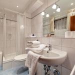 Badezimmer mit Dusche, Waschbecken und Toilette. Weiße Fliesen und Handtücher.