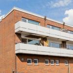 Two-story apartment building with balconies and red brick facade under blue sky.