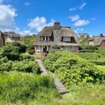 Dorfhaus mit Strohdach und Gartenweg unter blauem Himmel.