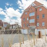 Rotes Backsteinhaus mit Dachgauben und Garagen. Vordergrund: Sand und Gräser.