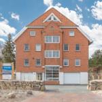 Rotes Backsteingebäude mit Garage und Dachgauben unter blauem Himmel.