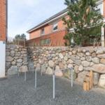Steinmauer mit Stufen und Metallgeländer. Hintergrund: Backsteinhaus mit Baum.