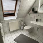 Helles Bad mit Dachfenster, Toilette, Dusche und großes Waschbecken mit beleuchtetem Spiegel.