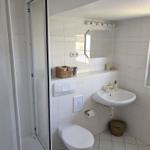 Badezimmer mit Dusche, Waschbecken und Toilette. Weiße Fliesen und Spiegelschrank.