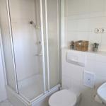 Badezimmer mit Dusche, Toilette und Waschbecken. Weiße Fliesen und kleine Pflanzen.