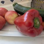 Auf einem Teller liegen Äpfel, eine Paprika, eine Zucchini und eine Karotte.