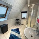 Helles Bad mit Dachfenster, Toilette, Dusche und großes Waschbecken mit beleuchtetem Spiegel.
