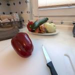 Küchenarbeitsfläche mit rotem Paprika, Messer und Gemüse auf Teller.