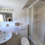Badezimmer mit Dusche, Waschbecken und Toilette. Weiße Fliesen und Spiegel.