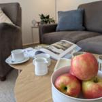 Tisch mit Äpfeln, Tassen und Zeitschriften vor einem Sofa