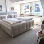 Schlafzimmer mit Doppelbett, Fenster und Sitzgelegenheit.