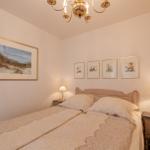 Schlafzimmer mit Bett, Nachttischen und Wandbildern.