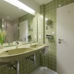 Badezimmer mit grünen Fliesen, Doppelwaschbecken und Spiegelschrank.